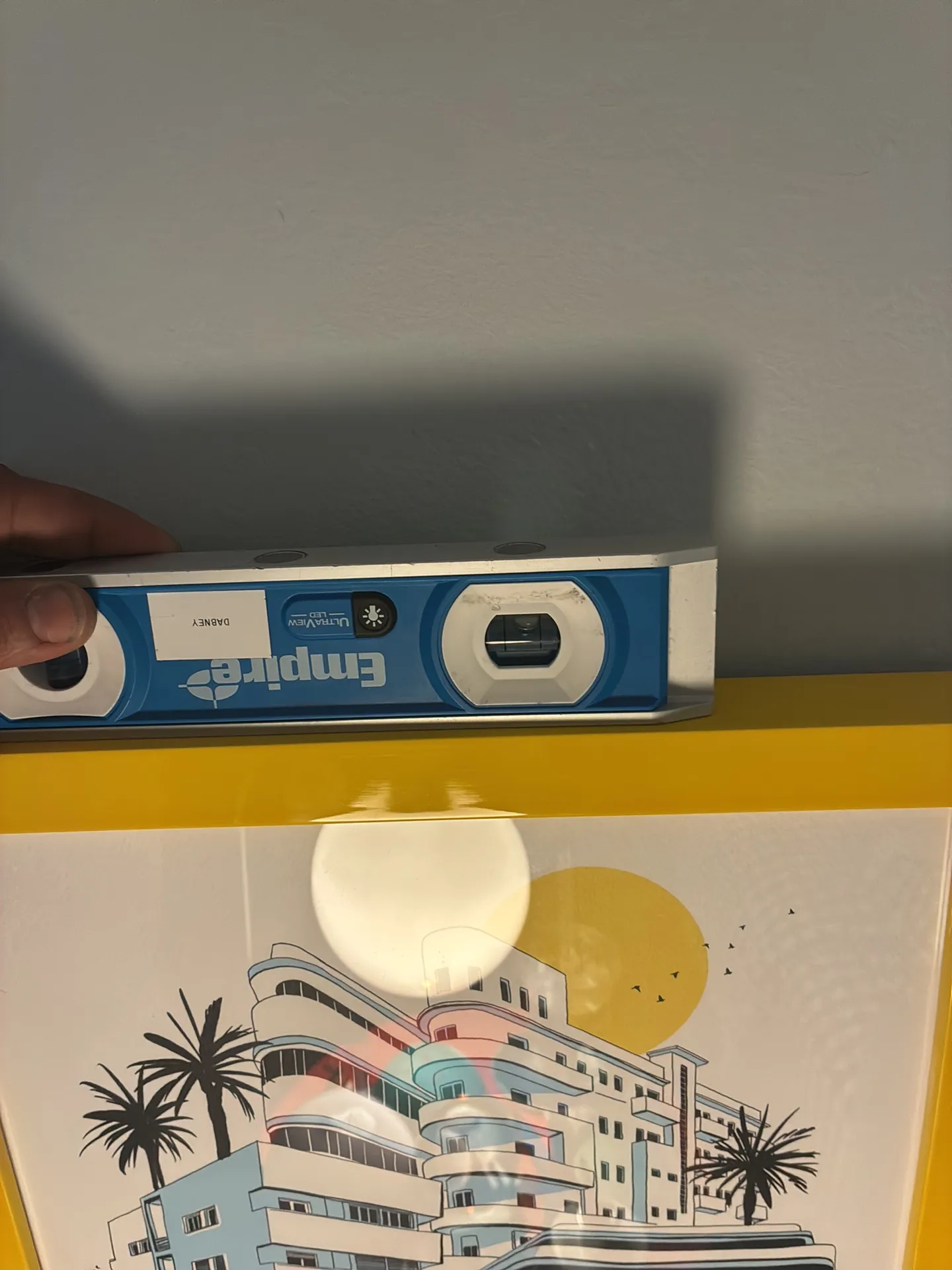 A spirit level rests on the top edge of a yellow-framed print.