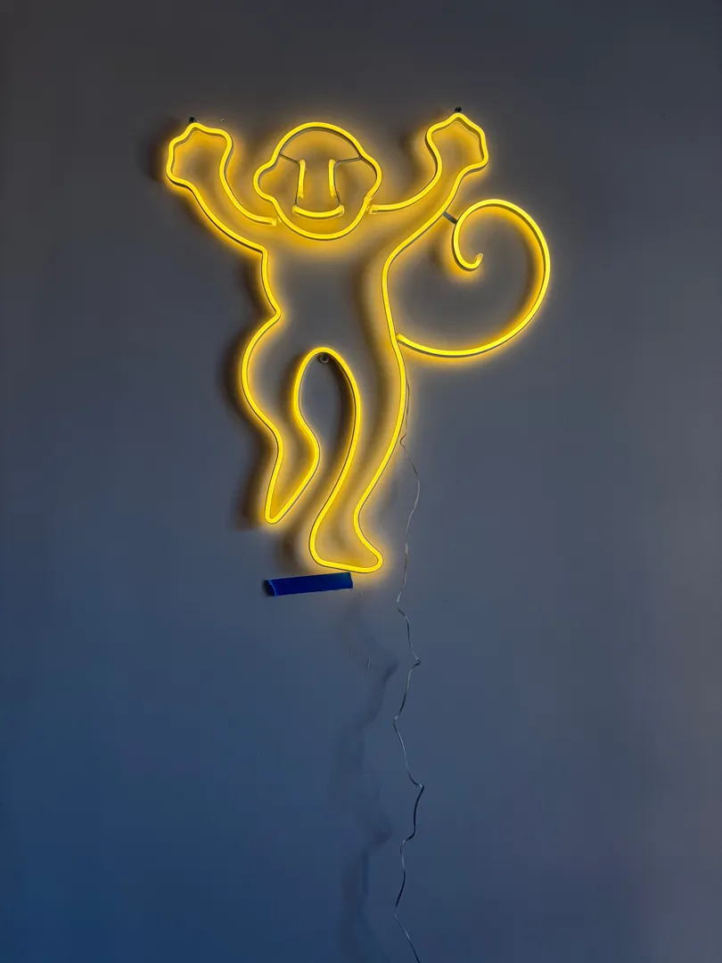 A yellow neon monkey sign mounted on a plain wall.