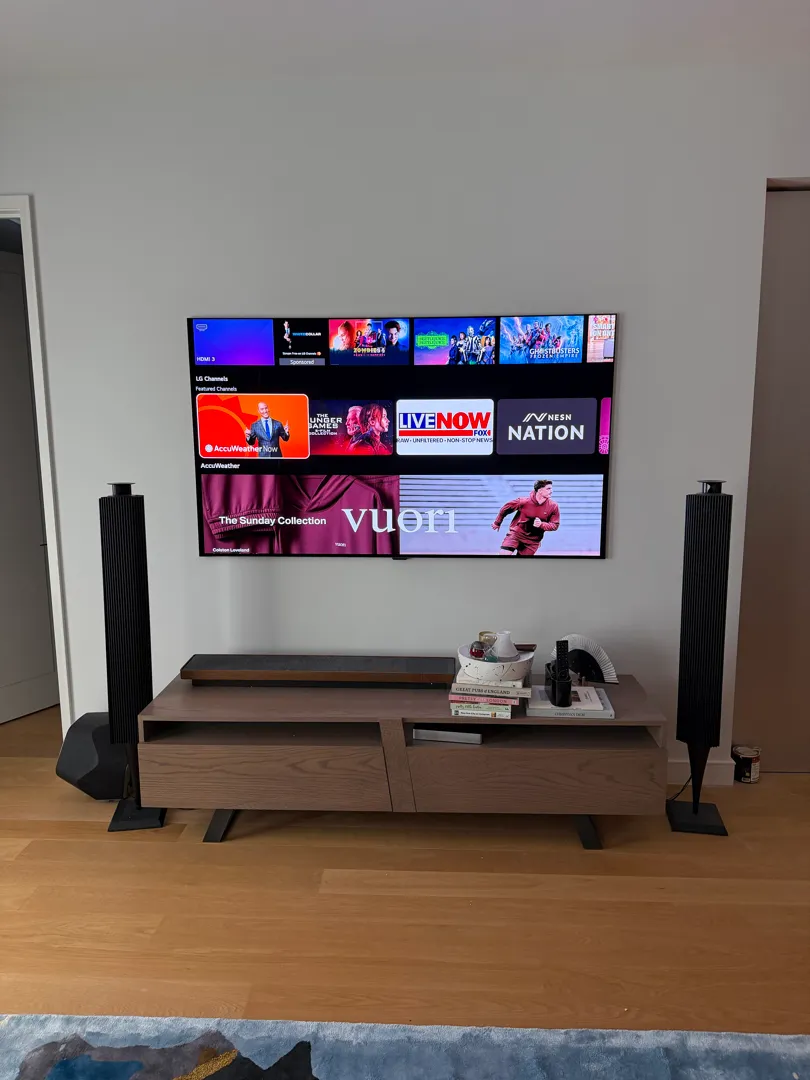 The 77-inch LG W6 wallpaper TV on the wall between two tower speakers, with no cable showing.