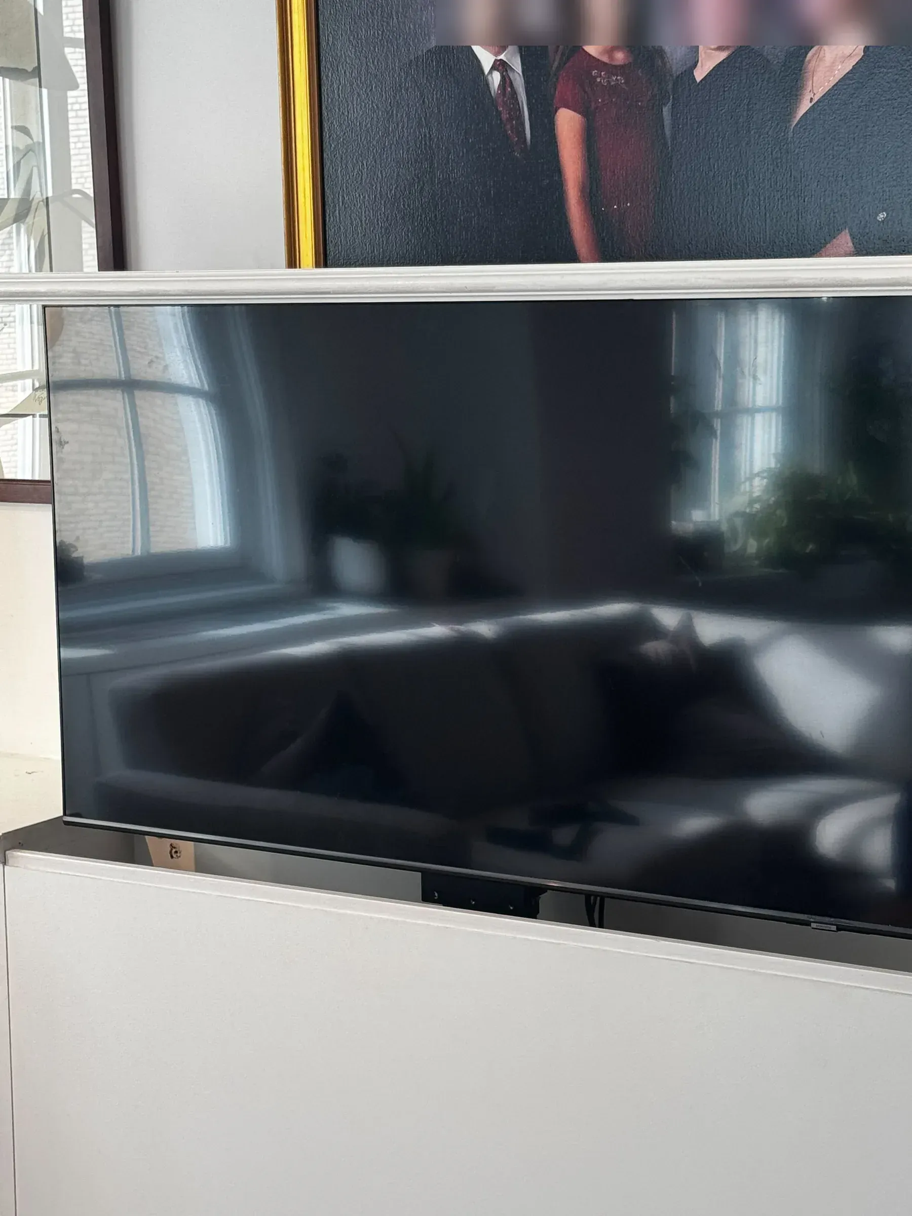 A close-up of the TV screen rising from the cabinet, with the family portrait visible just above it.