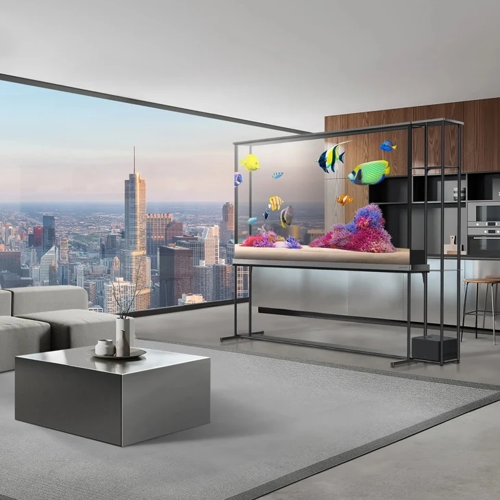 LG SIGNATURE OLED T standing as a room divider in a high-rise apartment, its transparent frame showing a tropical fish and coral scene with the city skyline visible through the glass behind it