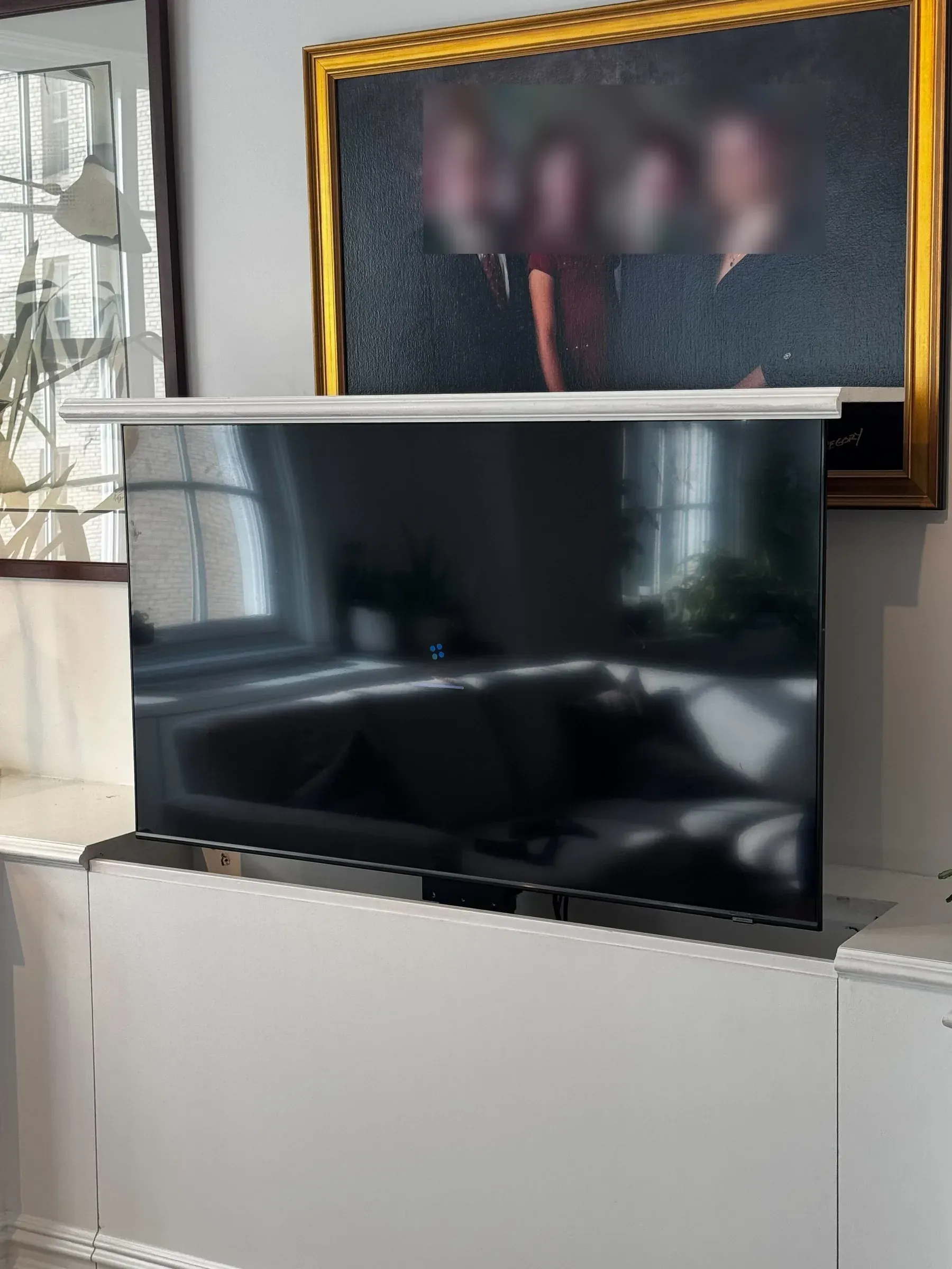 A flat TV sits raised above a white cabinet, with a framed family portrait mounted on the wall behind it.