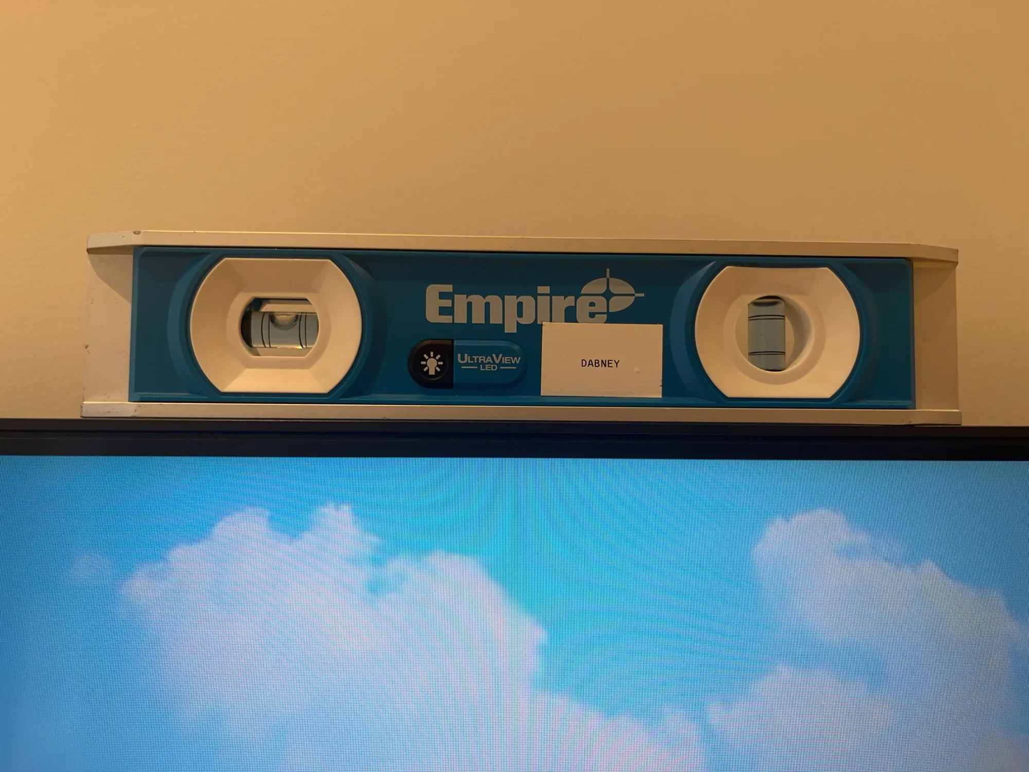 A blue bubble level resting on a TV screen, checking the mount is level.