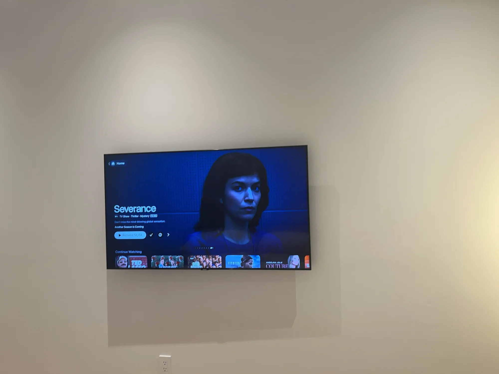 A flat-screen TV mounted flat on a bedroom wall, showing a streaming app home screen.