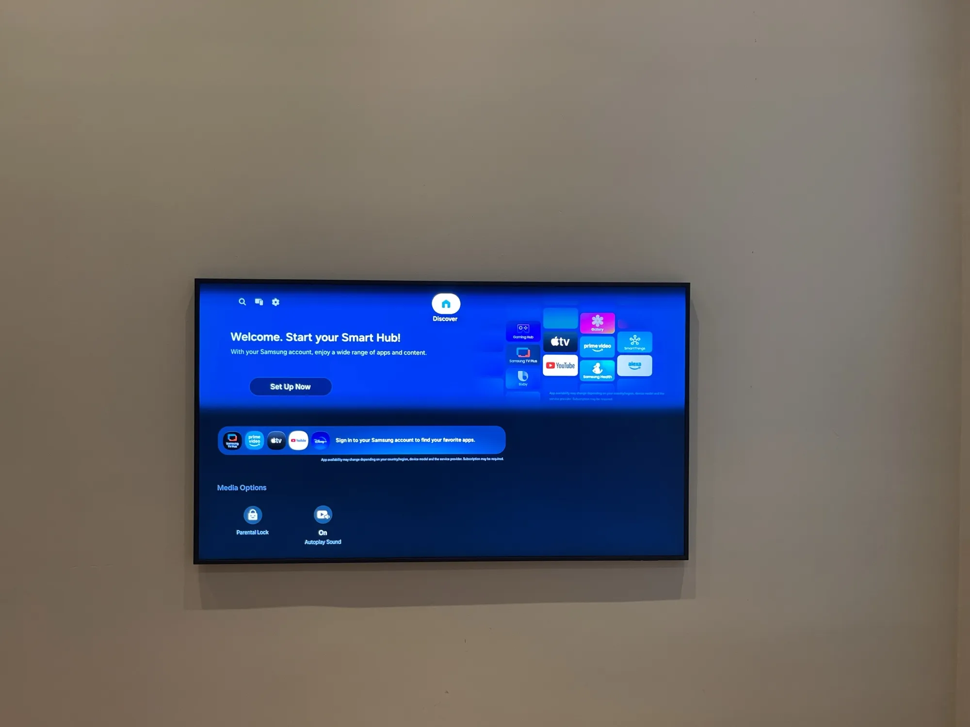 A wall-mounted TV showing the Samsung Smart Hub welcome screen.