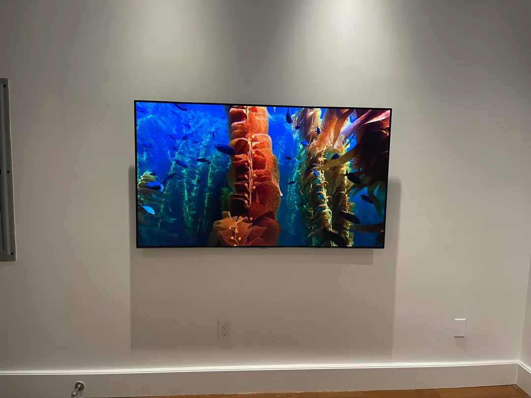 A flat-screen TV is mounted on a white wall with no visible cables, above two wall outlets.