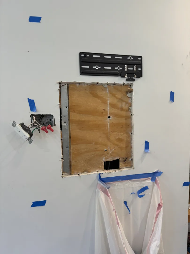 Rectangular wall opening below a Frame TV mount plate with a nearby power switch.