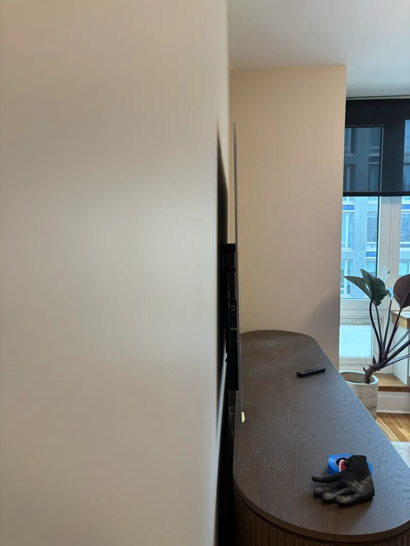 A TV on a wall mount seen edge-on above a dark wooden console, with a work glove and blue tape on top.