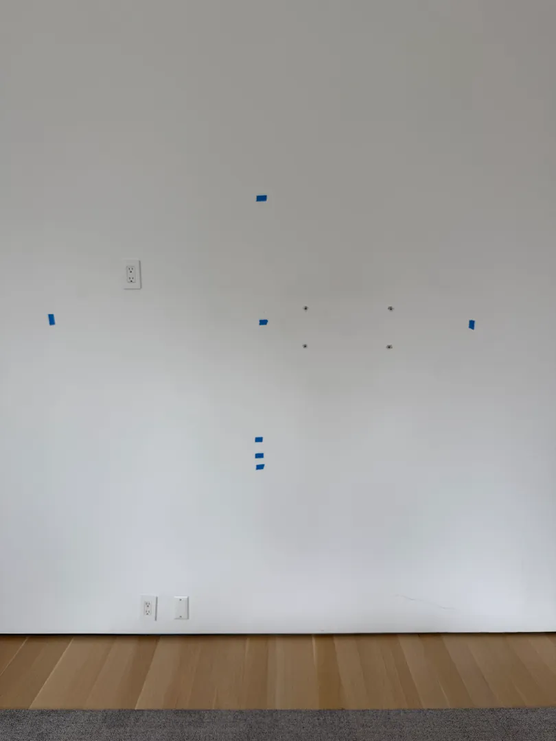 A bare white wall with blue tape marks setting out where the TV and soundbar will go.