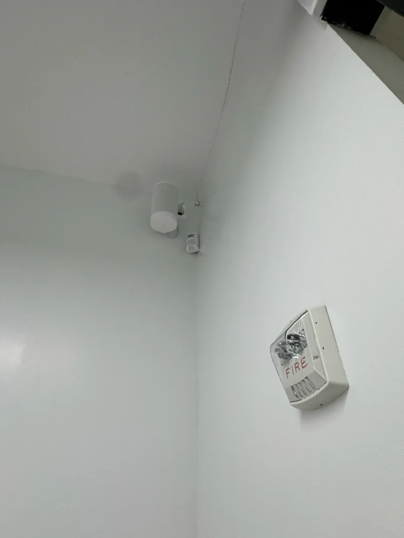 A small white speaker mounted high in the corner of a white office room.