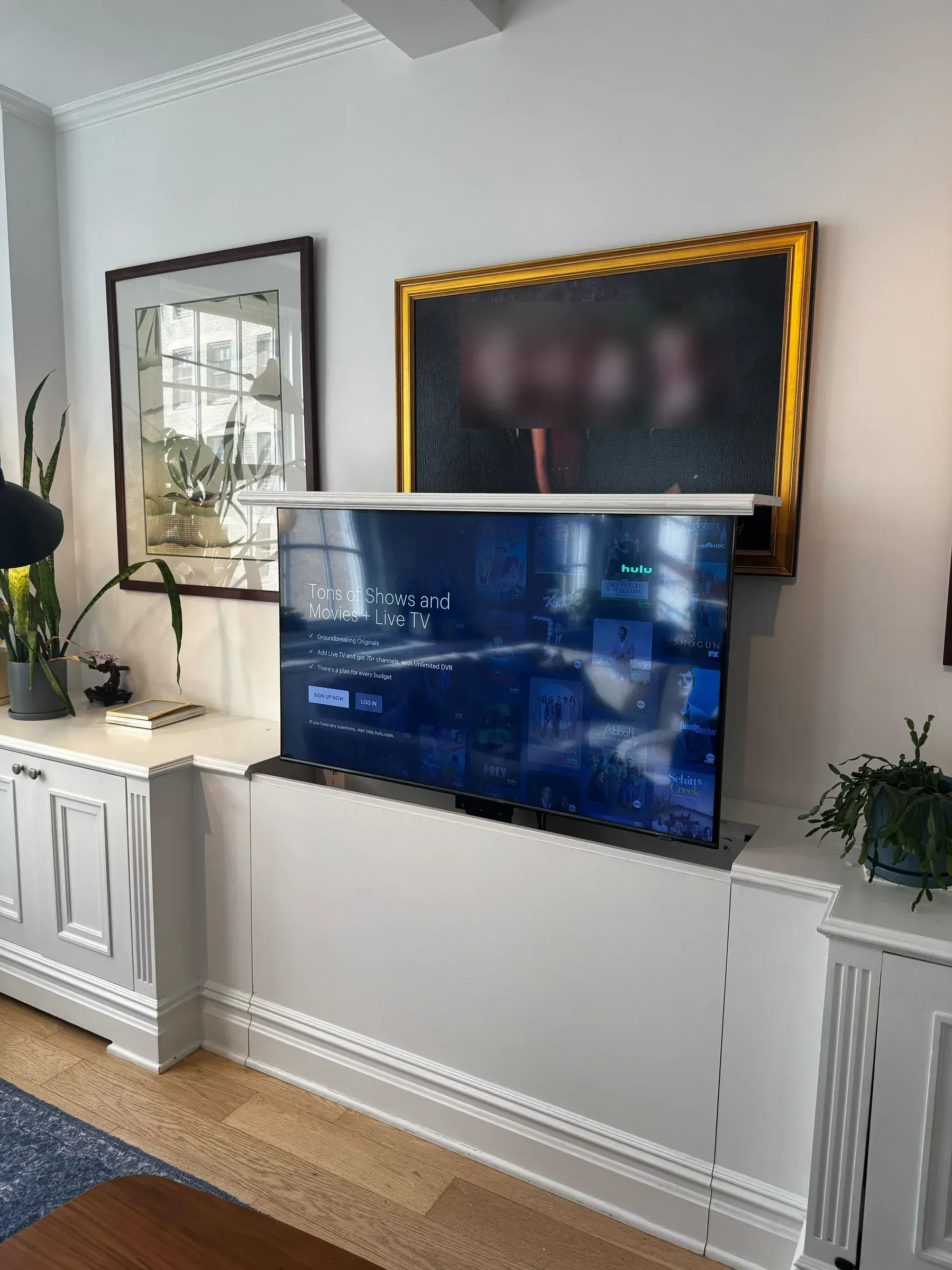 A TV powered on and showing a streaming home screen, raised above a cabinet below the family portrait.