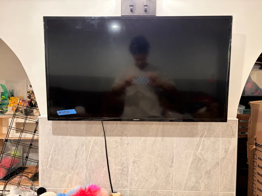 A TV mounted above a light stone-tile fireplace surround, its screen off.