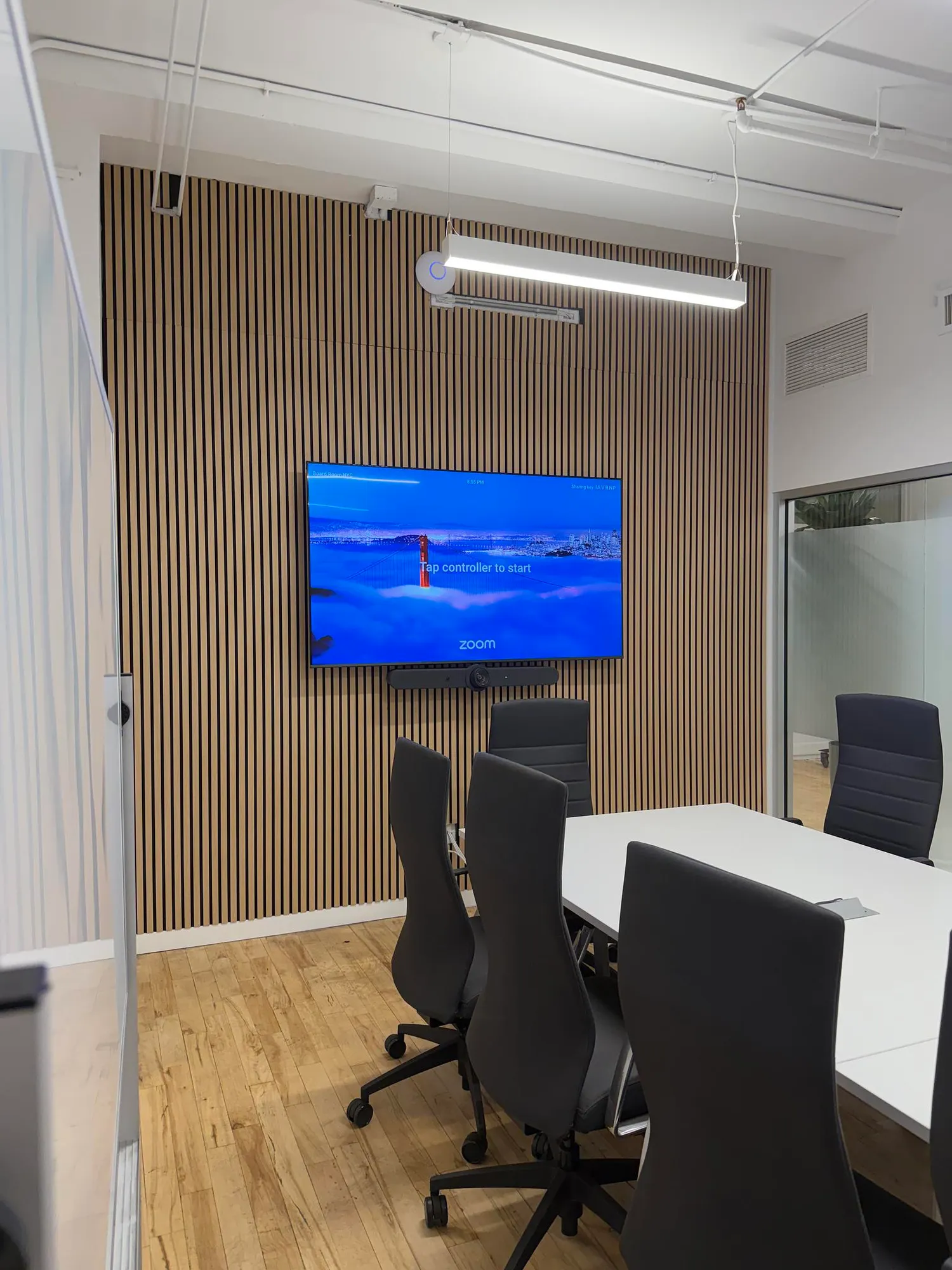 An angled view of a boardroom's wood panel wall from the doorway, next to a glass partition wall.