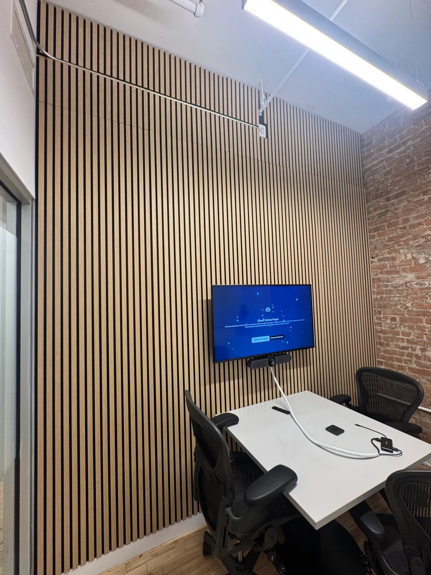 A tall angled view of a room with an exposed brick wall and a TV mounted on a wood panel wall.