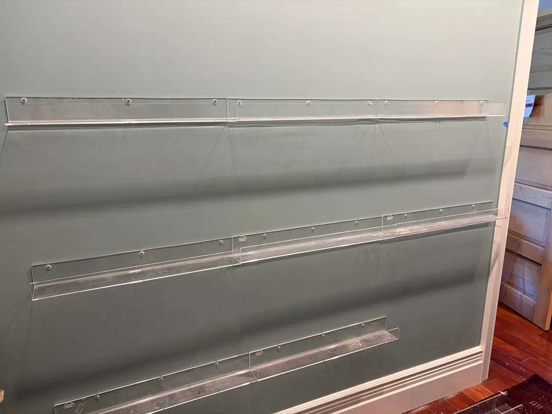 Three clear acrylic display ledges mounted in tiers on a wall.
