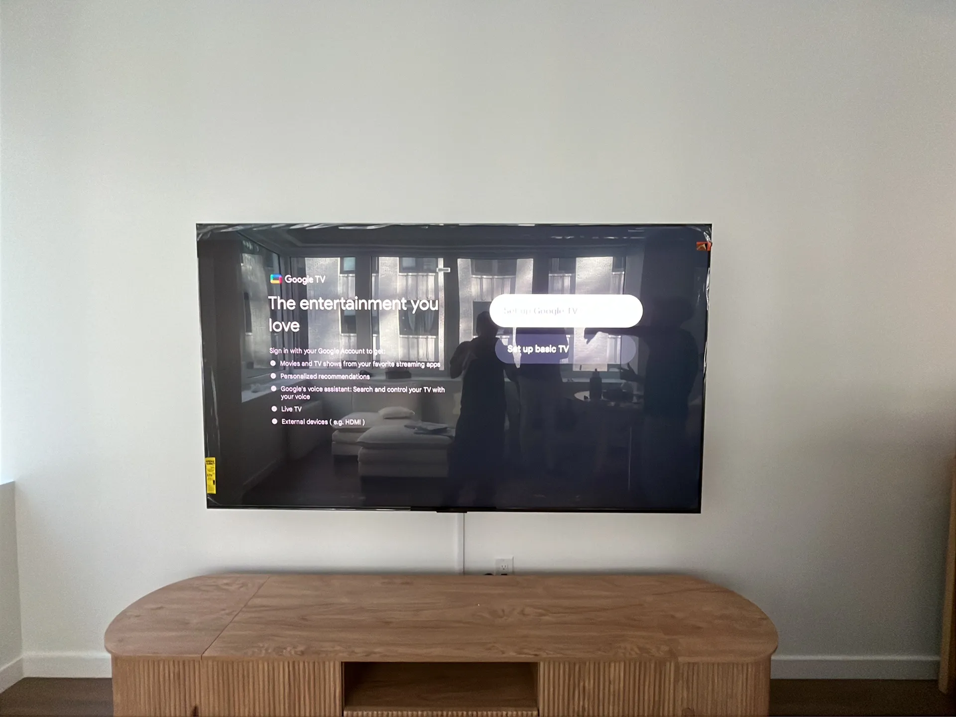 Wider view of the same wall-mounted TV showing the Google TV setup screen above the wood credenza.