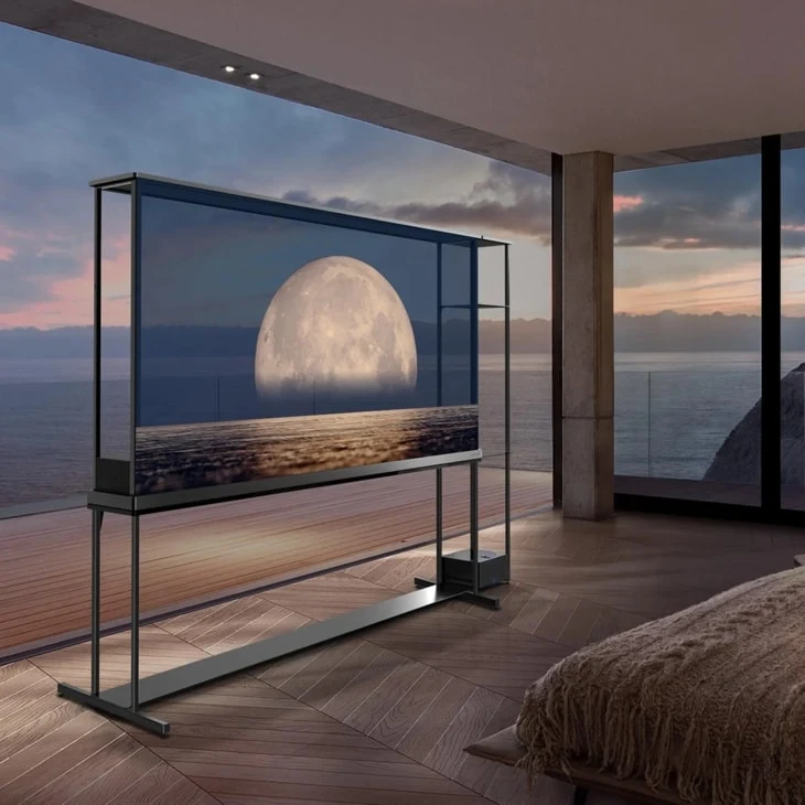 LG SIGNATURE OLED T on its stand in a bedroom at dusk, floor-to-ceiling windows showing an ocean view, screen displaying a glowing moon over water that blends into the real horizon