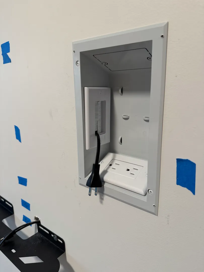 An angled view of the recessed outlet box with its power cable plugged in behind where the TV will sit.