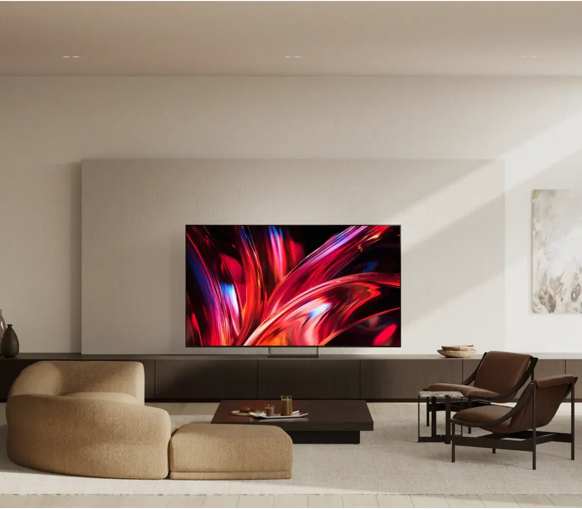The BRAVIA 9 II mounted on a wall above a low media console in a warm, modern living room with a curved sofa and leather armchairs.