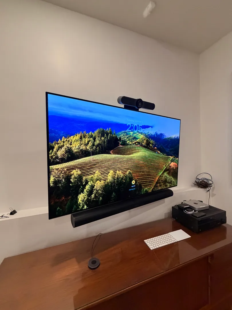The office TV after the visit, mounted on its full-motion arm with the video conference bar above it and the Sonos soundbar below, over the wooden credenza.
