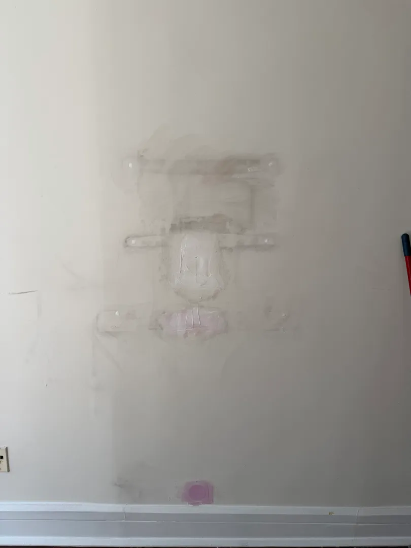A wall shows several patched spots of spackle compound covering old mount holes, not yet painted, with a light switch below a