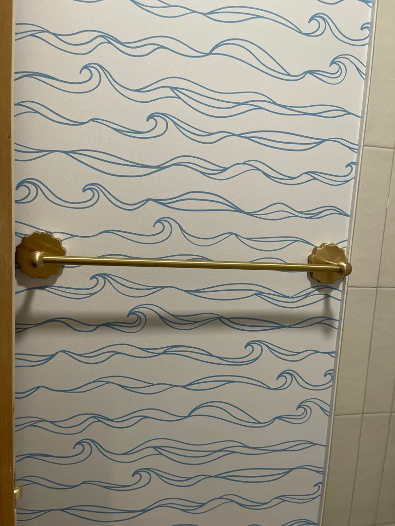 A gold towel bar mounted on wave-patterned wallpaper.