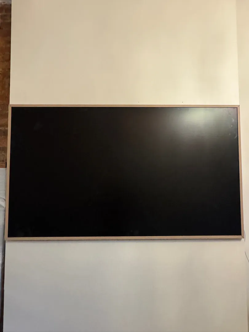 A large dark flat panel mounted on a wall next to an exposed brick wall.