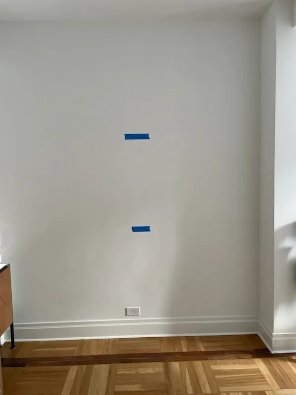 An apartment wall with two strips of blue painter's tape marking TV mount positions above an outlet.