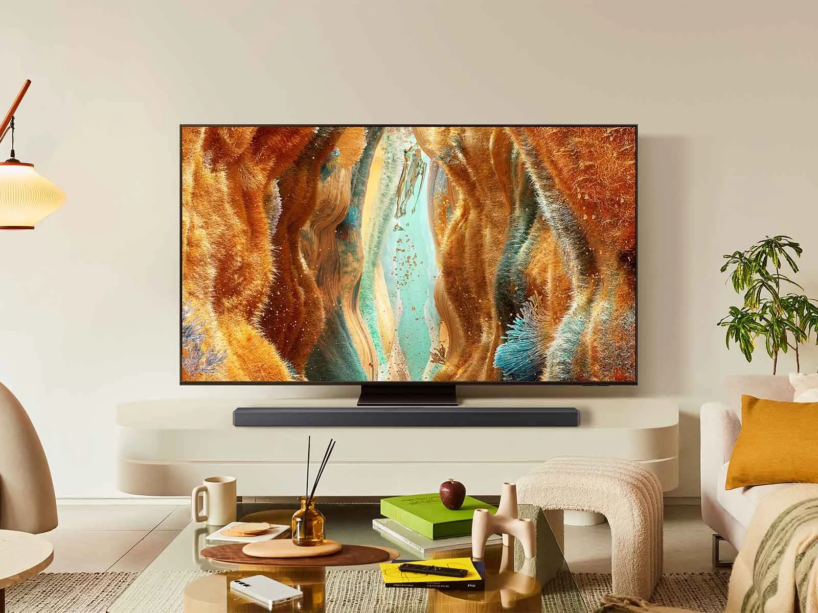 Samsung QN70F mounted above a soundbar in a warm, modern living room with a plant and coffee table