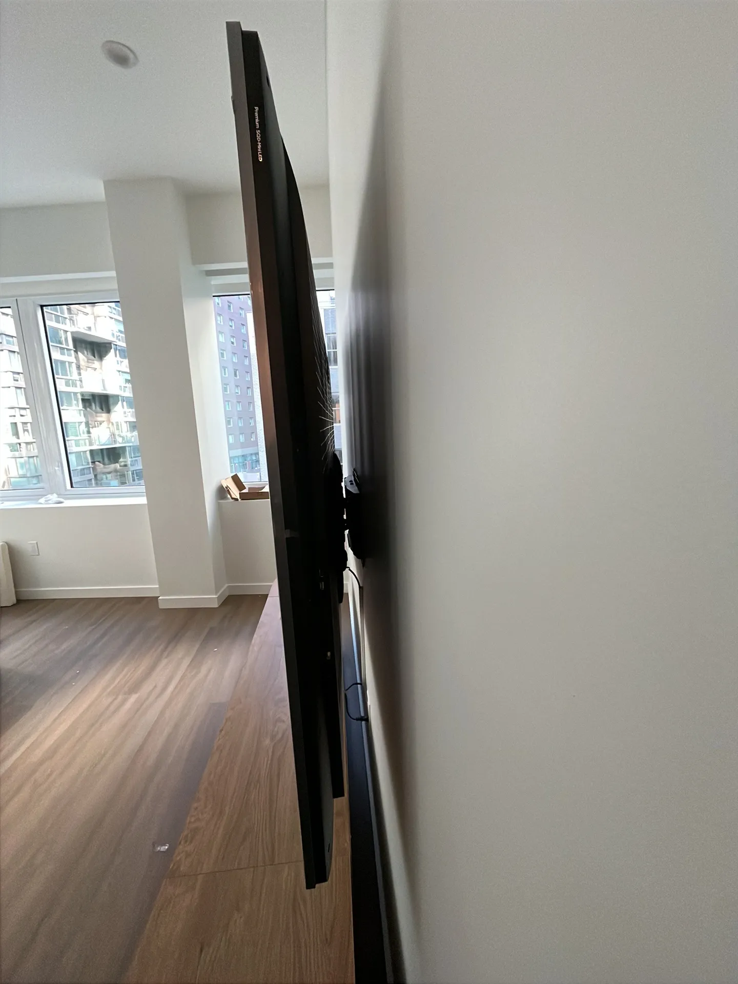 Side view of a TV on a full-motion wall mount in an empty apartment, still wrapped in plastic film, with cables hanging.