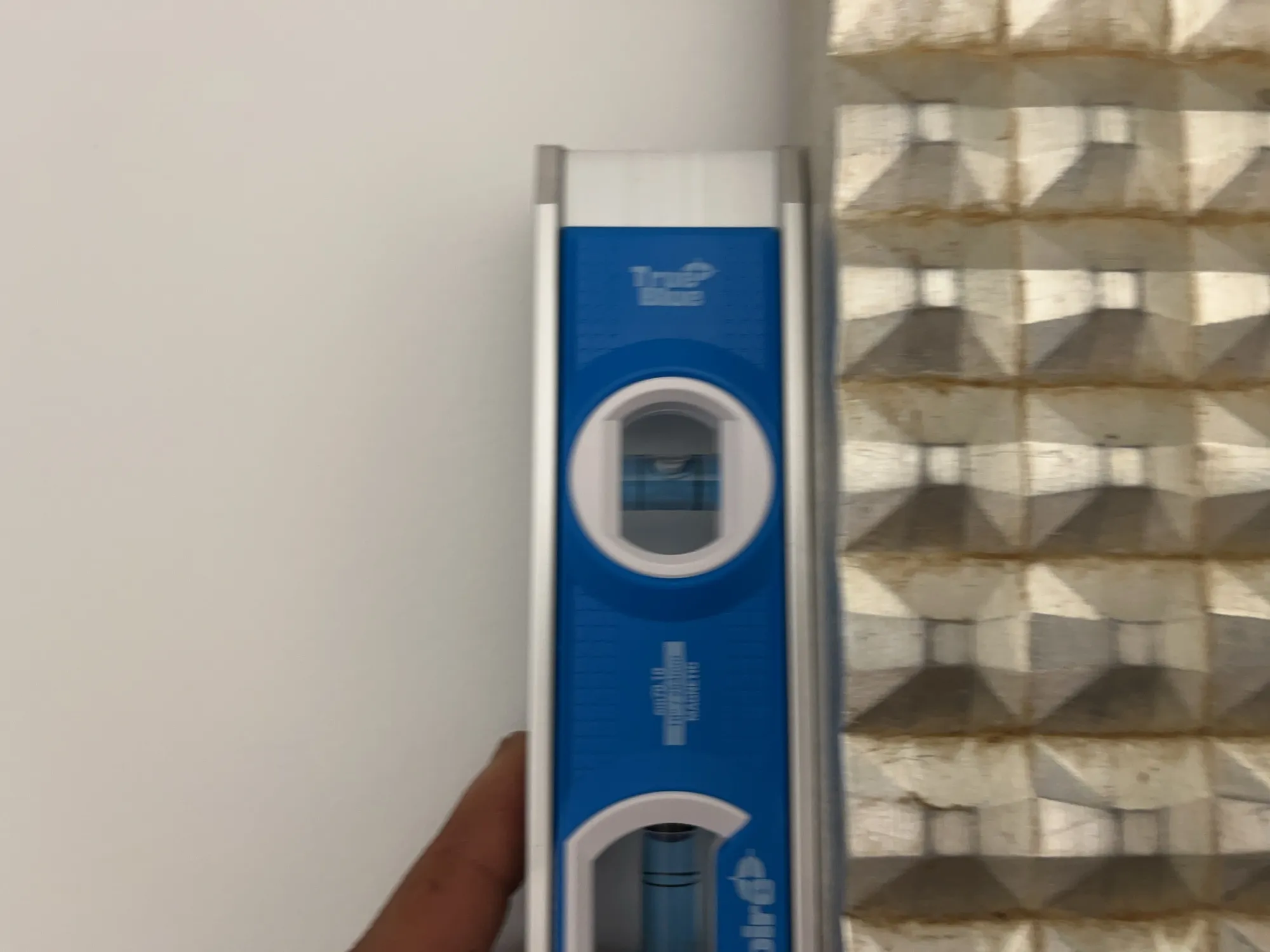 A level tool held against a wall beside a textured panel surface.