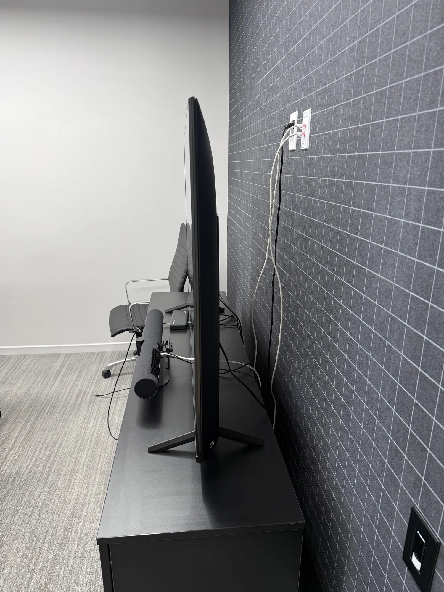 Side view of a TV resting on its stand on a desk, with several cables running from the back of the TV up the wall to an outle