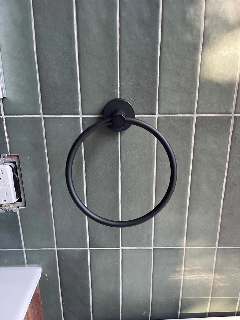 A black towel ring mounted on green bathroom tile.