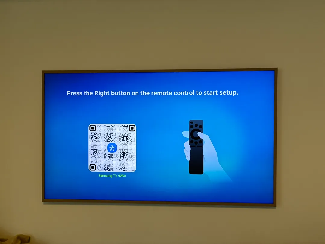 A wood-framed Samsung TV hanging on a wall showing a setup screen and a remote.