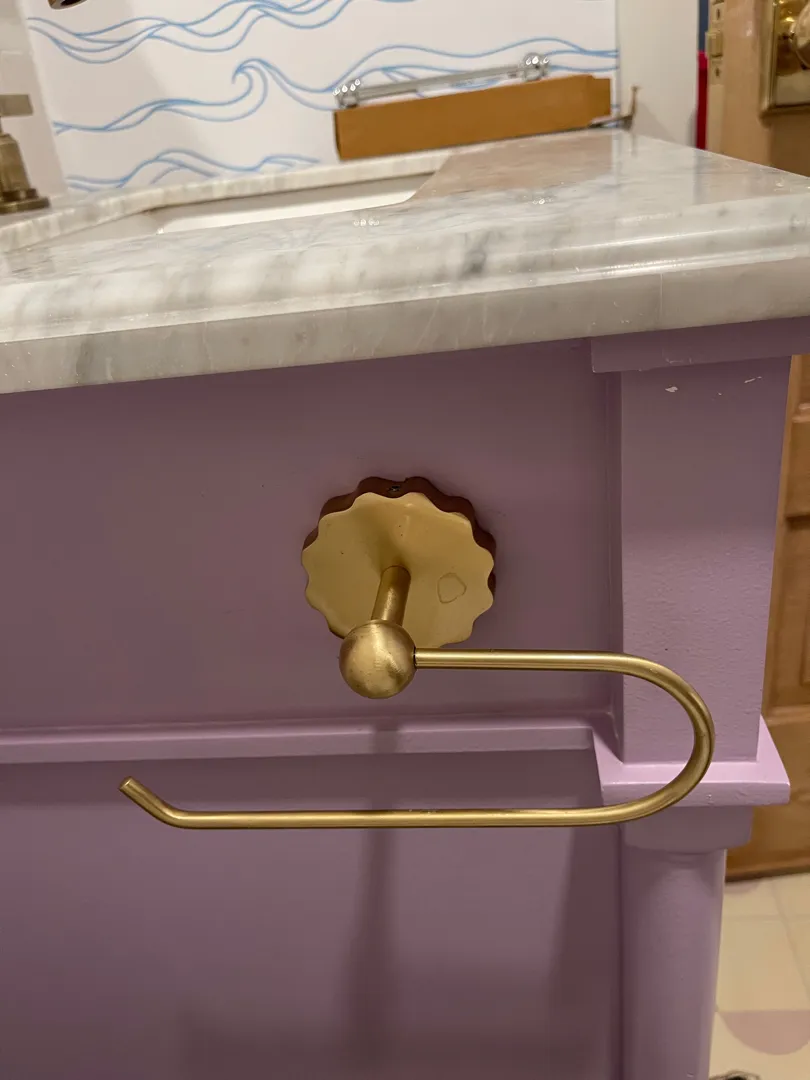 A gold toilet-paper holder mounted on a lavender bathroom vanity.
