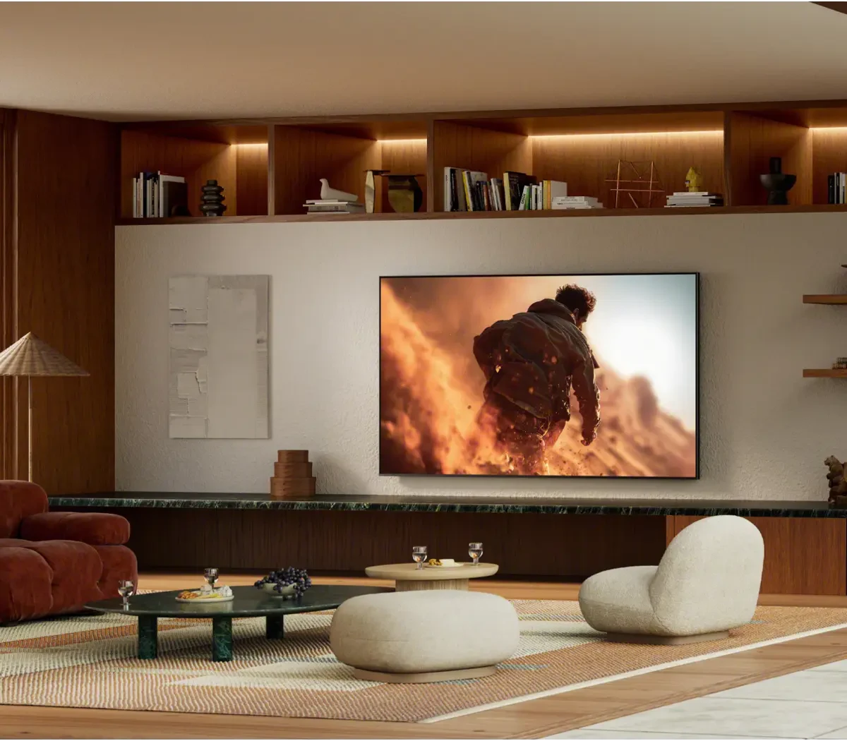 The BRAVIA 7 II mounted on a wall in a warm wood-paneled living room with built-in lit shelving, a rust-colored armchair and cream seating.
