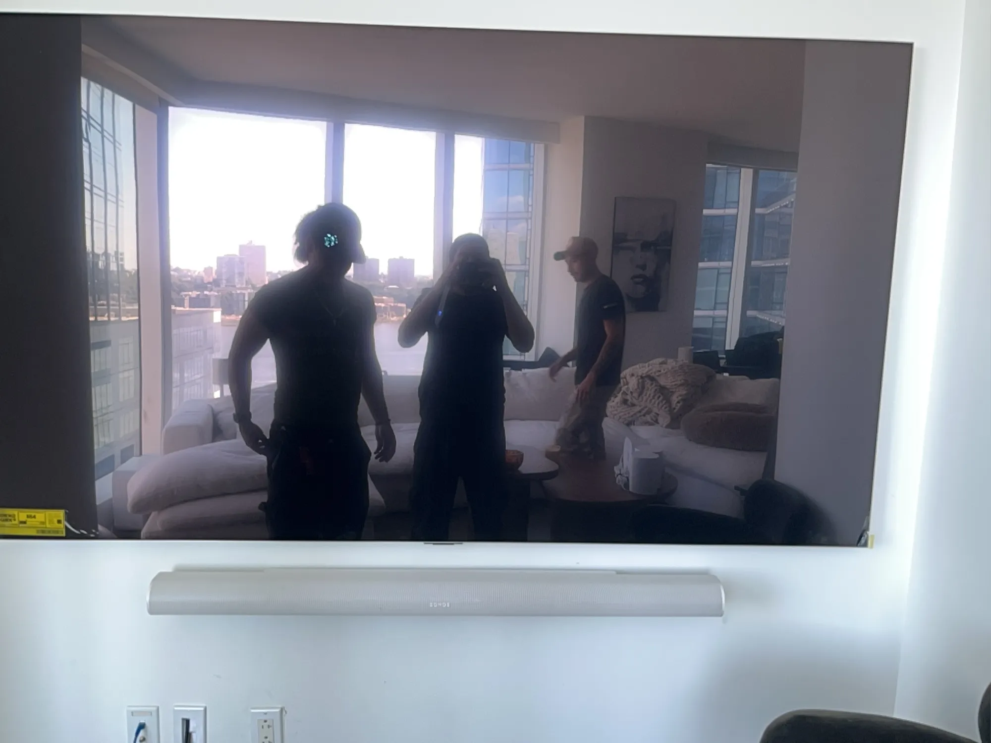 Reflection of the installation crew in the dark TV screen, with a price tag sticker and the Sonos soundbar below.