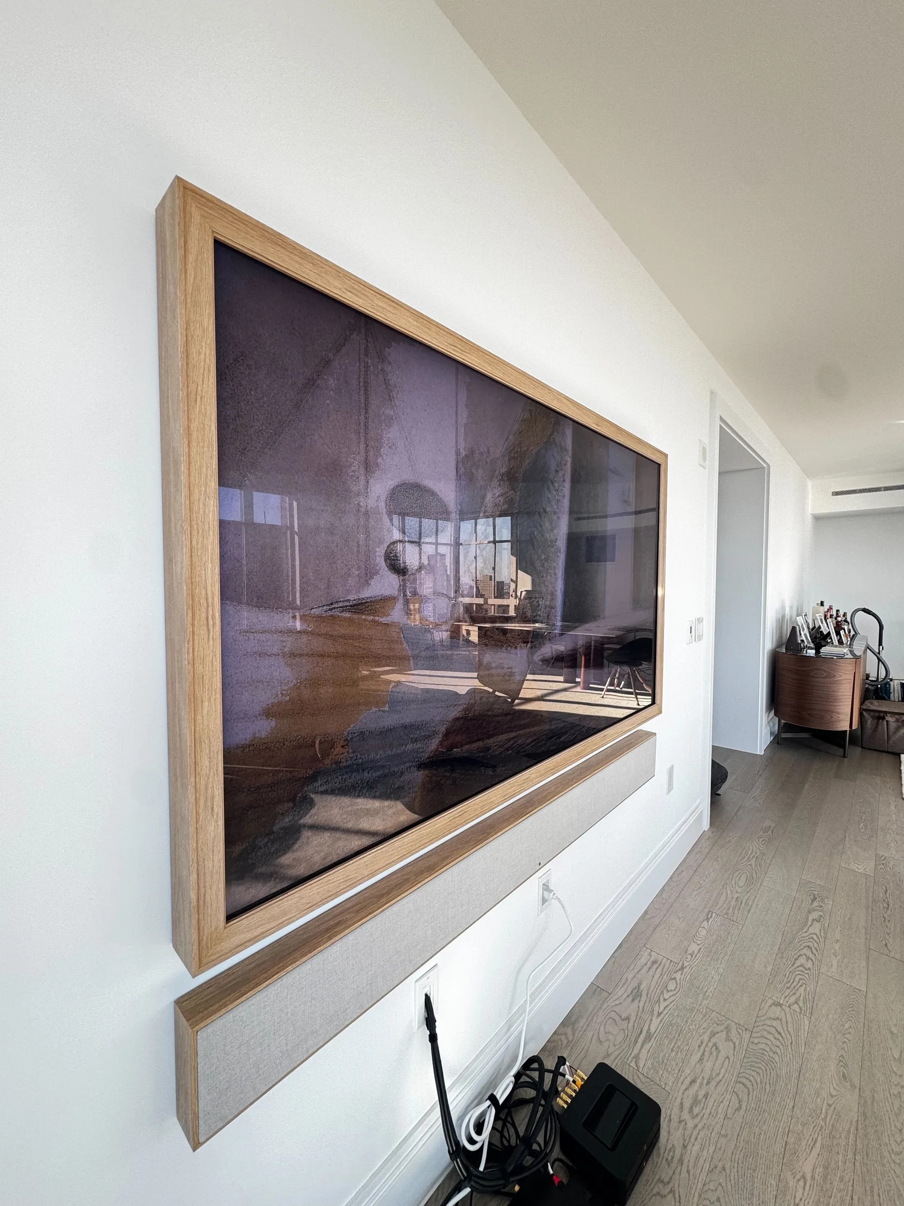 A TV in a light-oak wood frame, displaying a photo in Art Mode, with a matching framed soundbar mounted below it.
