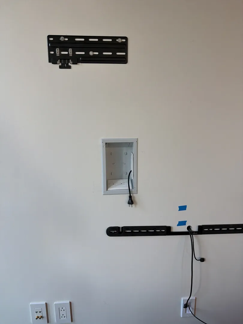 A TV wall plate, a recessed in-wall outlet box and a soundbar bracket on a white wall during the installation.