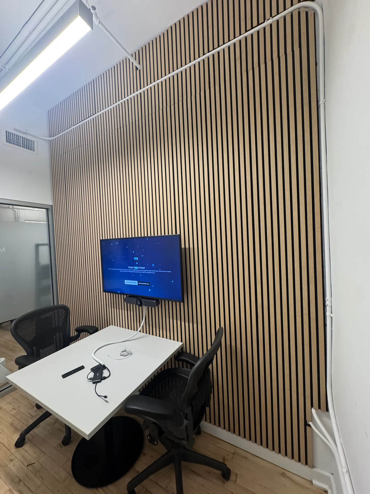 A small meeting room with an exposed brick wall and a TV mounted on a wood panel wall opposite it.