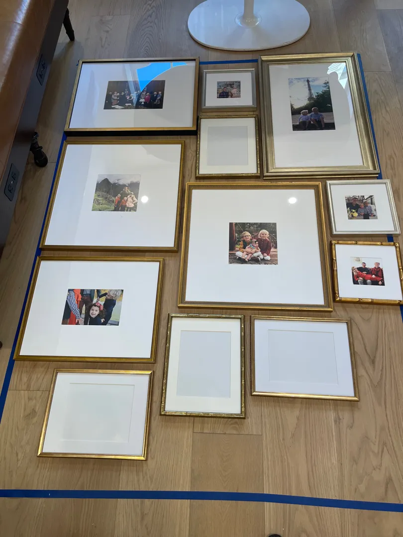 Twelve gold and silver picture frames arranged on the floor before hanging.