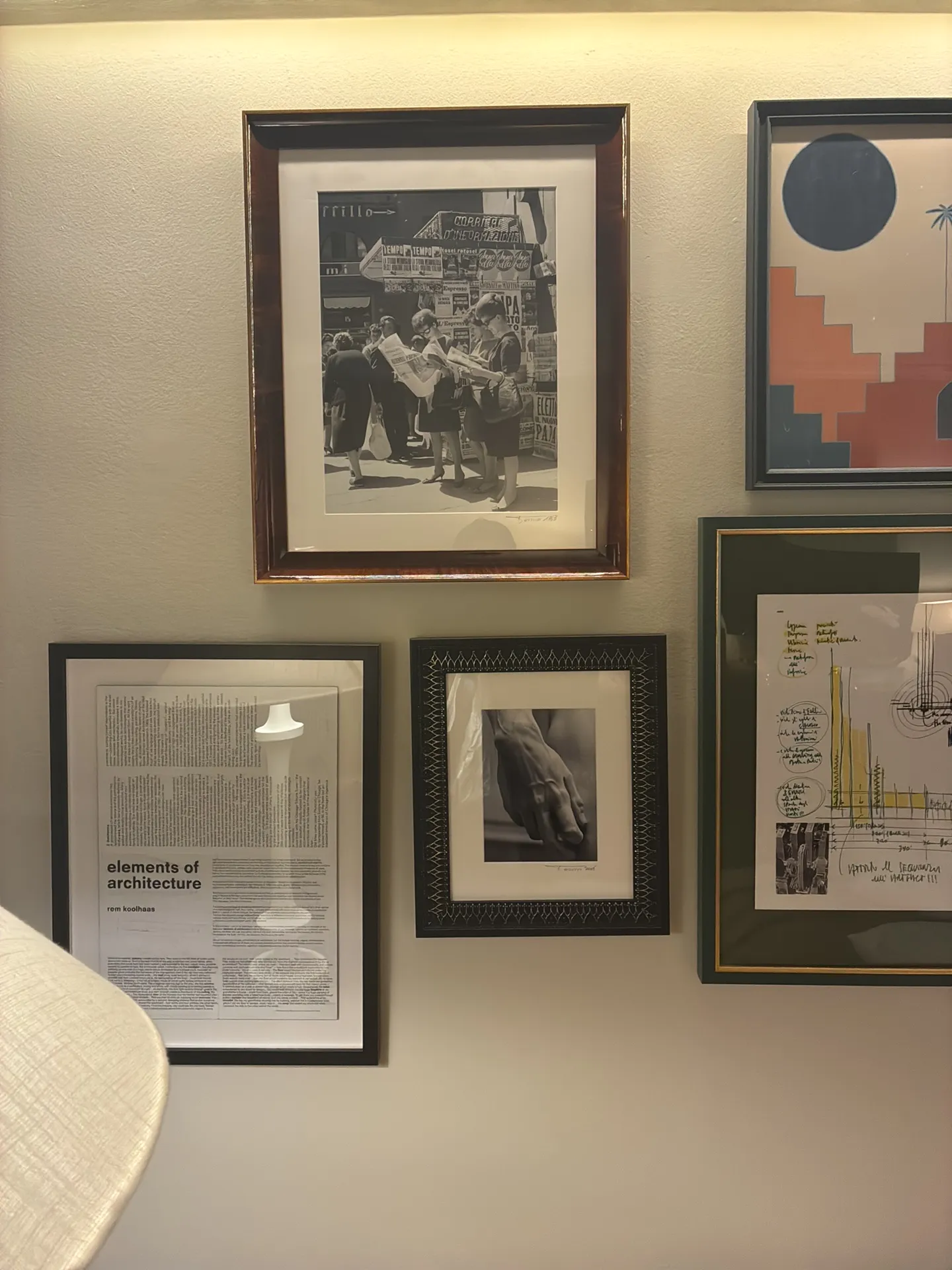 A group of framed black-and-white photos and prints on a cream wall under a warm light strip.
