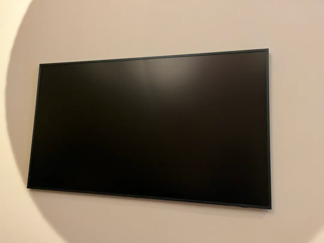 The mounted TV, screen off, flush against the wall, with the oval discoloration patch behind it.