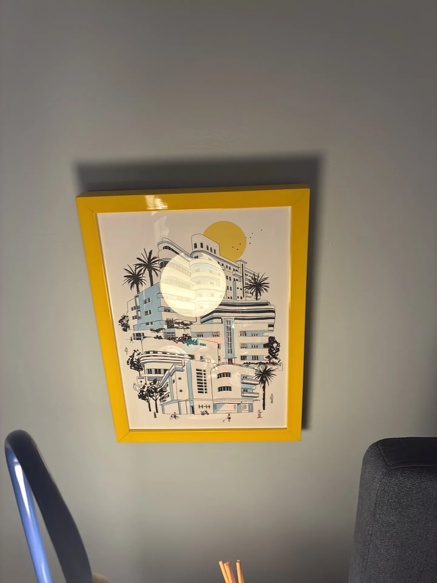 A yellow-framed building illustration hangs on a grey wall above a chair.