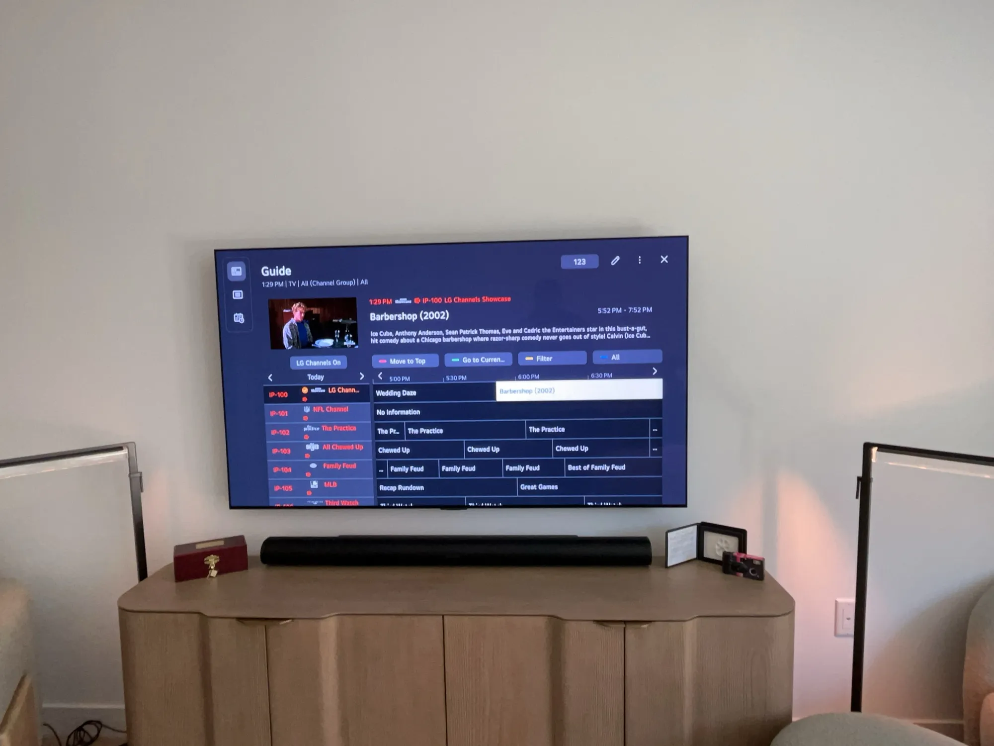 A wall-mounted TV showing a channel guide above a soundbar and media console with decor.