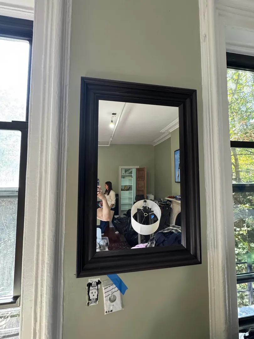 A rectangular dark-wood-framed mirror mounted between two tall windows.