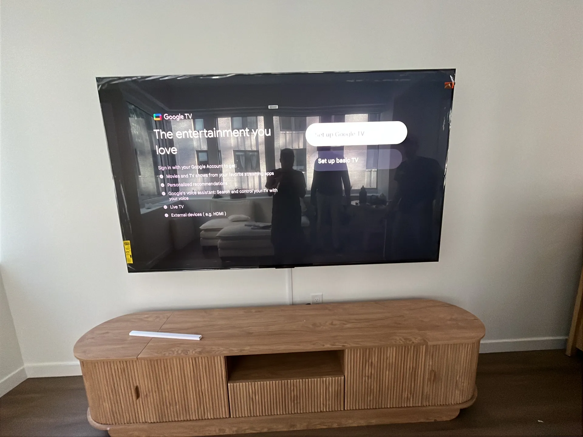 wall-mounted TV displays the Google TV setup screen above a wood credenza, with protective film strips still on the.