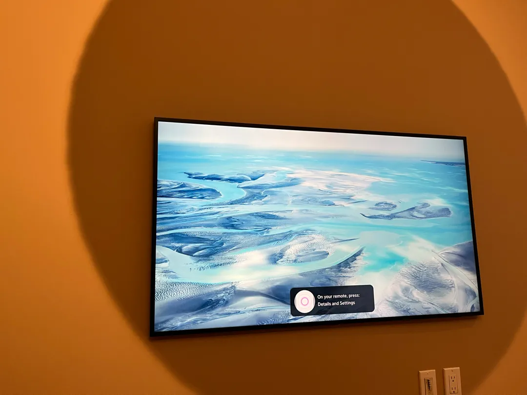 The mounted TV showing an ambient landscape image with an on-screen setup prompt, on the wall with the oval patch.