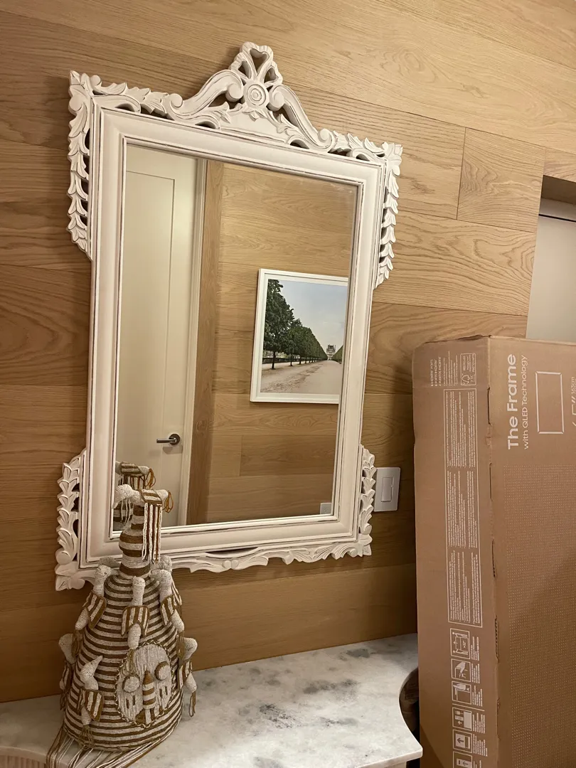Ornate white mirror mounted on a wood-panelled wall above a stone console.