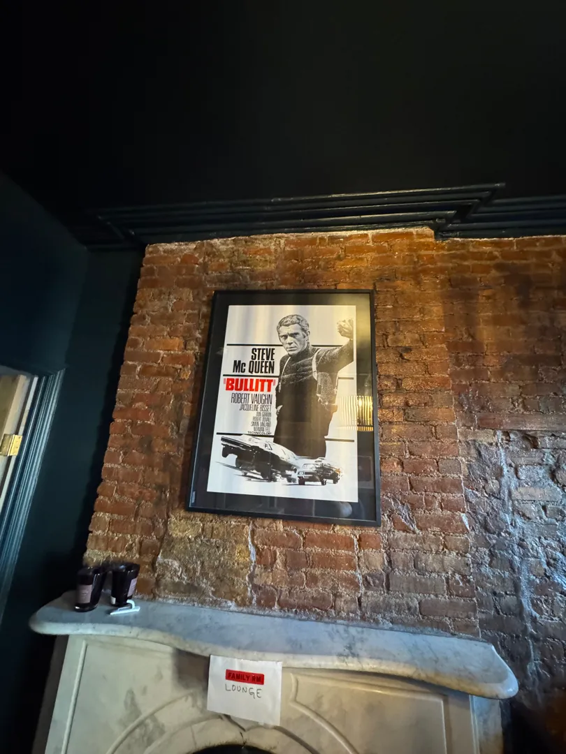 A framed vintage movie poster mounted on an exposed brick chimney breast above a marble mantel.